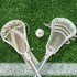 A white lacrosse ball positioned between two white lacrosse sticks on artificial grass.