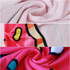 A custom-shaped beach towel featuring a pink background with vibrant patterns in red, yellow, and blue, showcasing its soft texture.