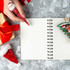 A red pen featuring a Santa stress reliever, surrounded by gifts, a blank notebook, and festive decorations.
