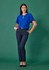 A model wearing navy tapered adjustable waist pants paired with a blue top against a green background.