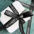 A gift box wrapped with black ribbed fabric ribbon, featuring a logo. The background is a textured green surface.