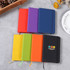A collection of PU A6 notebooks in various colours: red, purple, green, orange, and black, with an emblem on one.