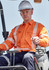A man wearing an orange hi-vis shirt with segmented reflective tape operates machinery while wearing a white hard hat and safety glasses.