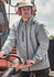 A man wearing a light grey unisex packable rain jacket, with a helmet and ear protection, operating machinery outdoors.