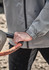 A close-up of a grey unisex packable rain jacket, focusing on the cuff and hand gripping a tool handle.