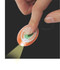 A hand pressing an orange press-light keyring, emitting light. The keyring features a logo on its surface.