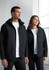 A black rain jacket is worn by a man and a woman, both posing indoors near a window. The jacket features a hood and has a logo.