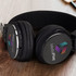 A pair of black Bluetooth headphones with a logo and control buttons, resting on a wooden surface.