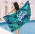 A sublimated beach towel featuring vibrant green leaves on a navy background, with the phrase "hello Summer" and a logo.