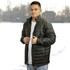 A puffer jacket in dark green, featuring a high collar and zip closure, worn by a model against a snowy background.