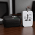 A white travel universal adaptor with a surge protector, placed alongside a black zip case featuring a logo.