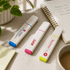 Three eco-friendly highlighters in blue, pink, and yellow on a desk next to a notepad and a plant.