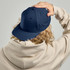 A navy blue cap with ventilation holes, worn backwards on a light-coloured hoodie. The cap features a logo.