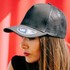 A black trucker cap with a mesh back and a logo on the front, worn by a model against a vibrant background.