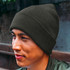 A dark green beanie is worn by a person with short hair, sitting outdoors with a blurred background.