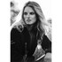 A woman with flowing blonde hair sits amid grass, wearing a black softshell jacket. The image is in black and white.