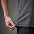 A close-up of a grey striped women's polo shirt, featuring a stylish split at the hem, being adjusted by a hand.