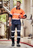 A man in orange and navy workwear with reflective stripes, holding a hard hat, stands in an industrial setting.