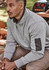 A man wearing a grey unisex 1/4 zip brushed fleece pullover with a logo on the sleeve, seated outdoors.