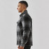 A men's plaid jacket in black and grey, featuring a Sherpa lining and a side view of the wearer. It has a logo.