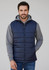 A man wearing a navy blue quilted alpine vest over a grey hoodie, with a casual expression.