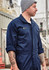 A man wearing a navy blue lightweight cotton drill overall with a logo on the chest, standing in an industrial setting.