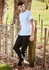 A person wearing black stretch jeans and a white t-shirt stands by a wooden fence in a grassy area.