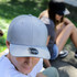 A grey cap with a logo sits in the foreground, while a person wearing a black cap is in the background.