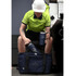 A blue drink bottle and mug sit next to a dark blue duffel bag, with a person in a high-visibility shirt and helmet.
