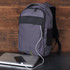 A grey laptop backpack with a sleek design, featuring a logo, resting on a table next to a laptop and phone.