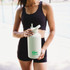 A drink bottle in light green with a flip-top spout, held by a person in activewear. It features a logo.