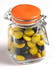 A glass clip lock jar filled with yellow and black choc beans, featuring an orange lid.