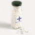 A tall glass jar with a black lid filled with white mints, partially spilled onto a light background.