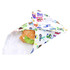 A reusable food wrap featuring a colourful design with letters and cartoon characters, tucked around a sandwich.