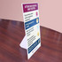 A freestanding sign in white and purple on a wooden table, displaying health check questions for patients and visitors.