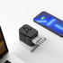 A black travel adaptor with multiple ports sits on a surface next to a smartphone, connected to various cables.