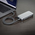 A silver Bluetooth speaker power bank with a textured surface, connected to a laptop with a braided cable.