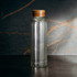 A drink bottle with a ribbed glass body and a wooden cap, featuring a clear colour against a textured background.