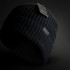 A black beanie with a ribbed texture and a tag attached, featuring a logo.