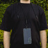 A phone lanyard in black, securely holding a smartphone around a person's neck against a green background.