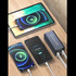 A black power bank with two cables, charging a tablet and two smartphones on a wooden surface.