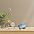 A multi-function phone stand in black, displaying a phone against a neutral background with a clock and flowers nearby.