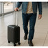 A black wheeled cabin trolley being pulled by a person in denim clothing, on a tiled floor in an airport setting.