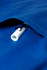 A close-up of a blue scrub top featuring a white zippered pocket. It has a logo visible on the fabric.