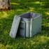 A grey cooler box with a detachable lid, positioned on grass, surrounded by outdoor scenery.