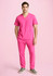 A unisex pink V-neck scrub top with two pockets, paired with matching pink pants and grey shoes.
