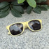 Colour changing sunglasses in a soft yellow frame resting on a stone surface, surrounded by green foliage.