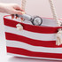 A hand holds a transparent cooling fan as it is placed inside a red and white striped tote bag.