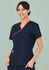 A navy scrub top with contrast red detailing, featuring a crossover design and pockets. The model is smiling.