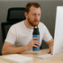 A drink bottle in blue and black, featuring a logo, is held by a person seated at a desk with a computer.